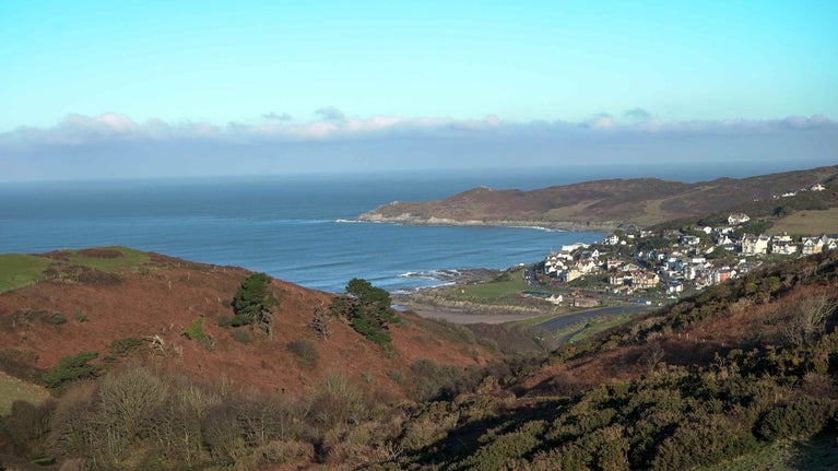 A scenic view of a small town by the ocean, captured from a hilltop, showcasing the coastline and surrounding landscape